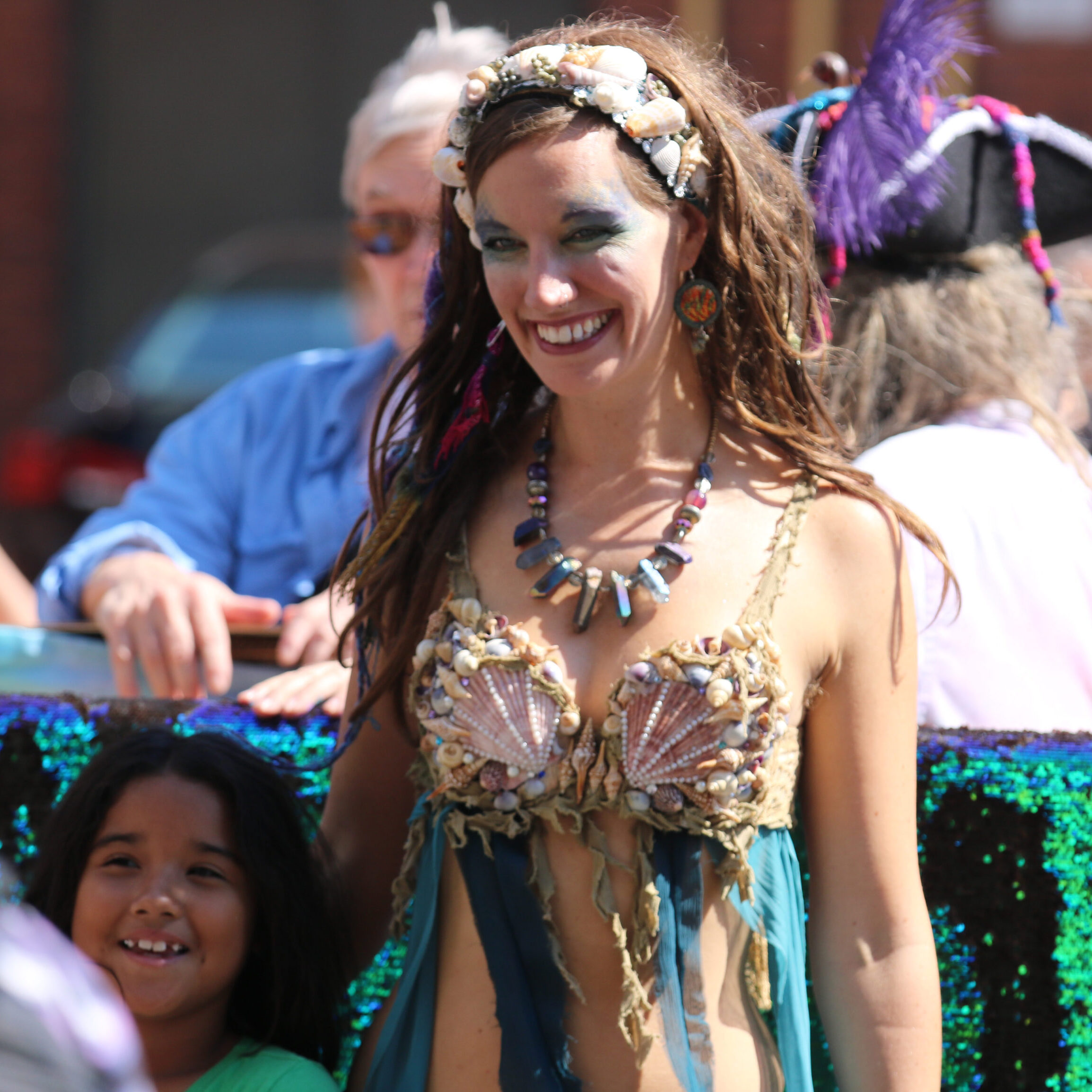 A woman dressed up as a mermaid standing beside a young child for a picture