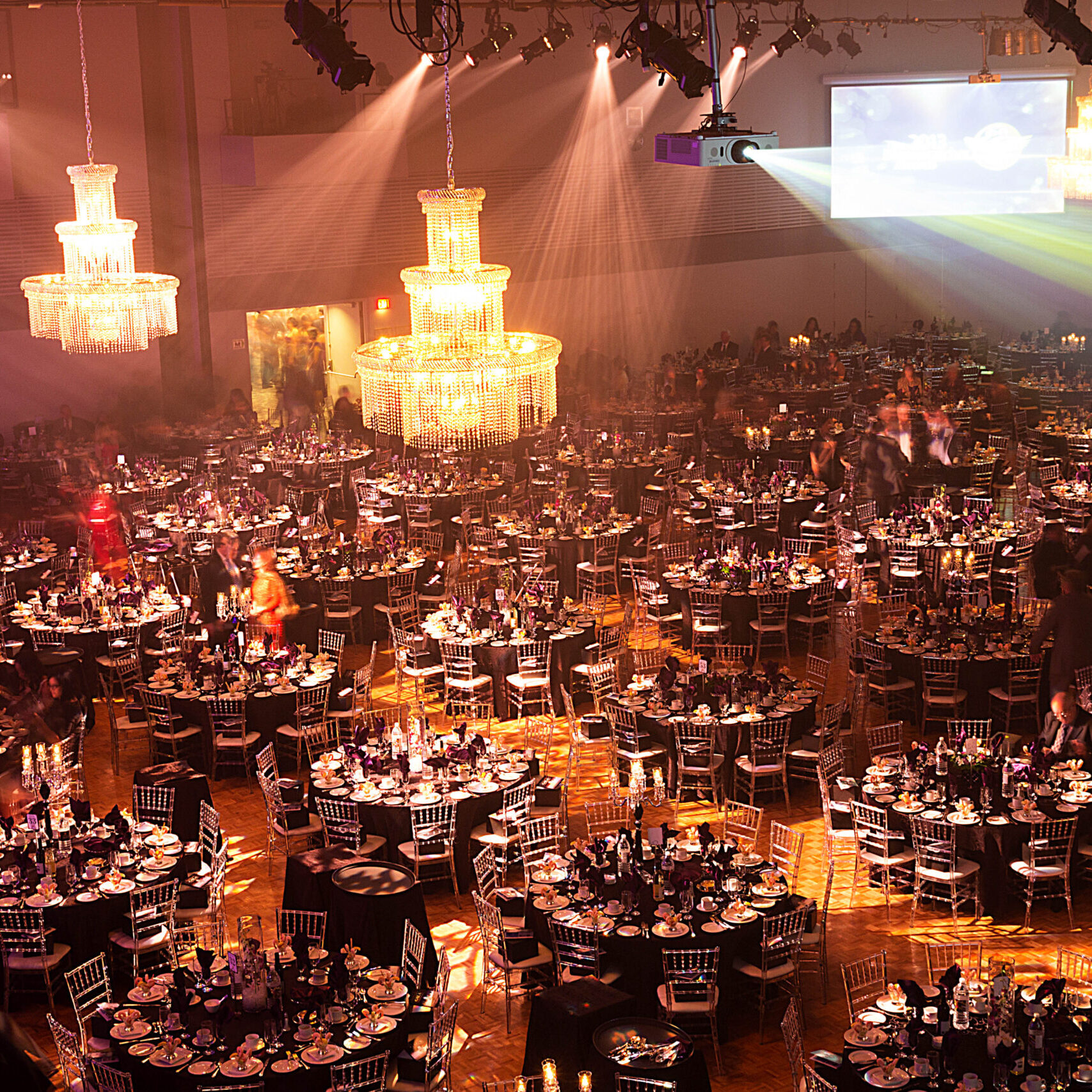 Looking down on a huge banquet hall full of round tables and hanging chandaliers