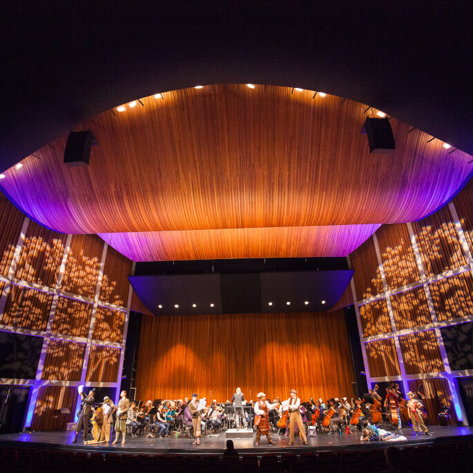 A stage in a theatre with an orchestra and 3 people singing